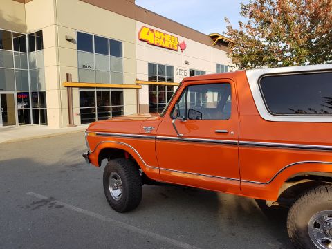 1978 Ford Bronco - An orange 1978 Ford Bronco is parked in front of a commercial building with a "4 Wheel Parts" sign. The vehicle is shown from the side, wit…
