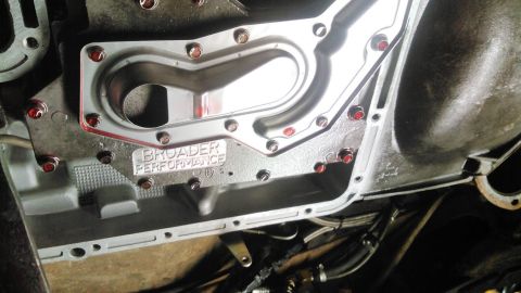 1978 Ford Bronco - A close-up view of a transmission pan with a polished metal gasket and red-capped bolts. The text "BROADER PERFORMANCE" is visible on the p…