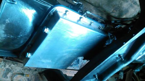 1978 Ford Bronco - A close-up, low-angle view of a shiny, silver transmission pan bolted to the underside of a vehicle. The pan appears to be a custom or afte…