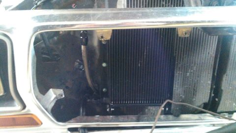 1978 Ford Bronco - The front of a vehicle's engine bay is shown, with the grille removed to reveal the radiator and an auxiliary cooler. The chrome grille sur…