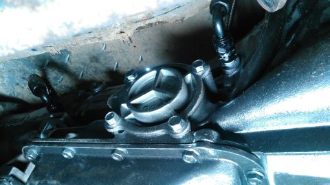 1978 Ford Bronco - A close-up view of the underside of a vehicle, focusing on the transfer case and transmission components. Several metal lines and fittings…