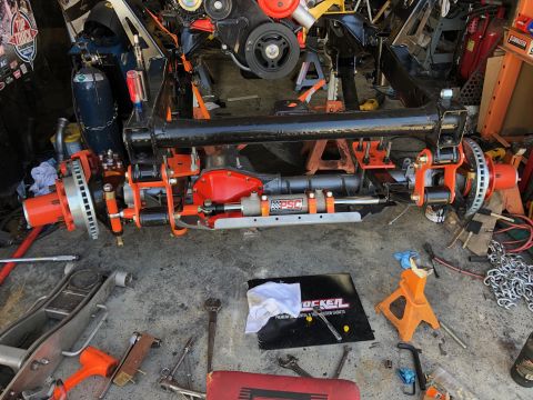 1992 Jeep Wrangler - A custom off-road front axle assembly with orange suspension components and disc brakes is laid out on a concrete floor, surrounded by tool…