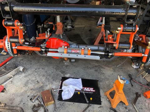 1992 Jeep Wrangler - A close-up view of a modified Jeep Wrangler front axle assembly with bright orange suspension components and a hydraulic steering assist cy…