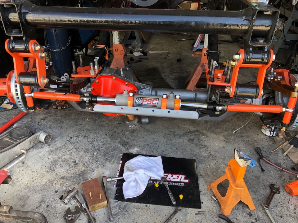 Modified Jeep Wrangler front axle with orange suspension and hydraulic steering assist.