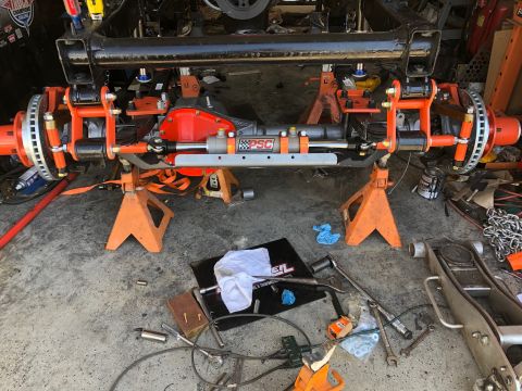 1992 Jeep Wrangler - A custom orange suspension and steering system is installed on the front axle of a vehicle, which is supported by orange jack stands. The s…