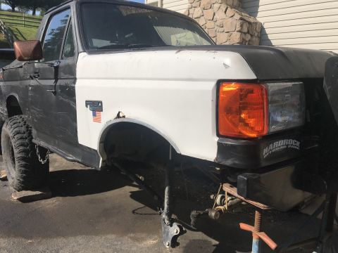 1989 Ford Bronco - Front fender and headlight assembly of a Ford F-Series truck, showing a white fender and black hood.