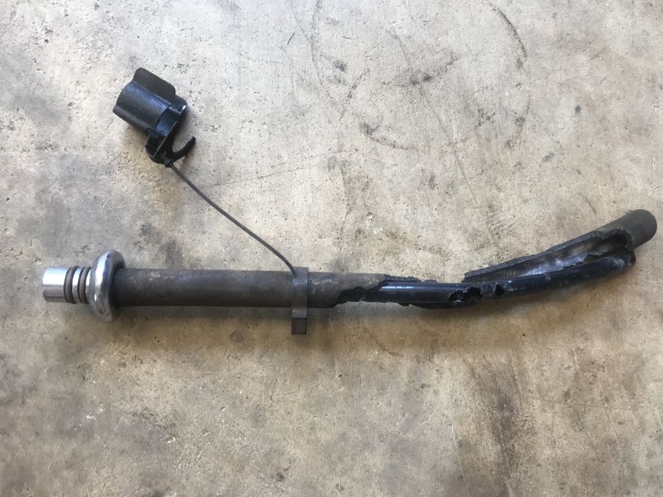 Damaged metal rod with a black electrical connector and wire attached, lying on a concrete surface