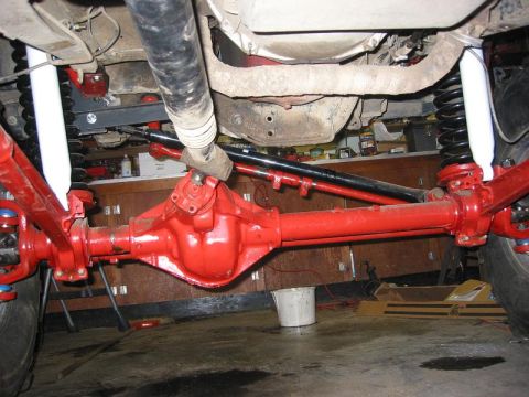 1985 Ford Bronco - Close-up view of a vehicle's undercarriage, highlighting a red-painted solid axle and suspension components.