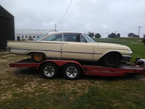 1961 Ford Starliner - A cream-colored 1961 Ford Starliner is transported on a red trailer under an overcast sky.
