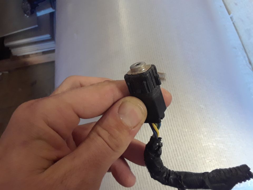 Hand holding a black electrical connector with yellow and blue wires, part of a wiring harness