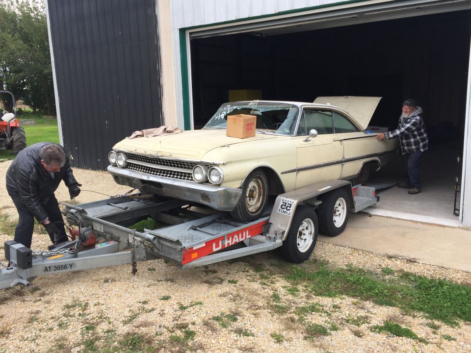 Cream 1960s coupe on trailer, front 3/4 view. U-Haul trailer visible