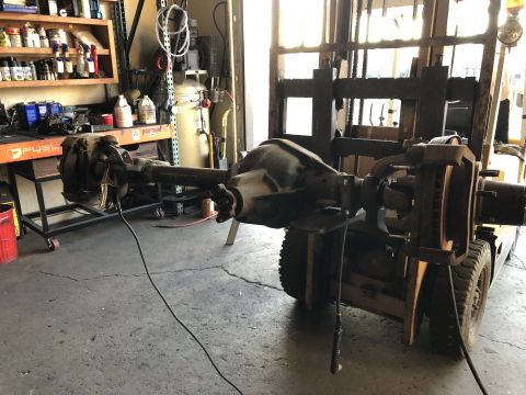 1986 Ford Bronco - Forklift moves a vehicle axle assembly in a workshop environment.
