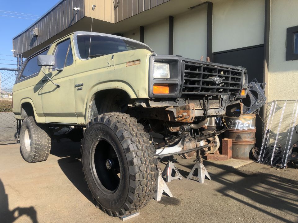 Light green Ford Bronco on jack stands, front end removed, large off-road tires