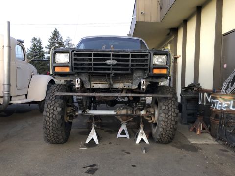 1986 Ford Bronco - Ford Bronco front end undergoing modifications, parked next to a large truck.