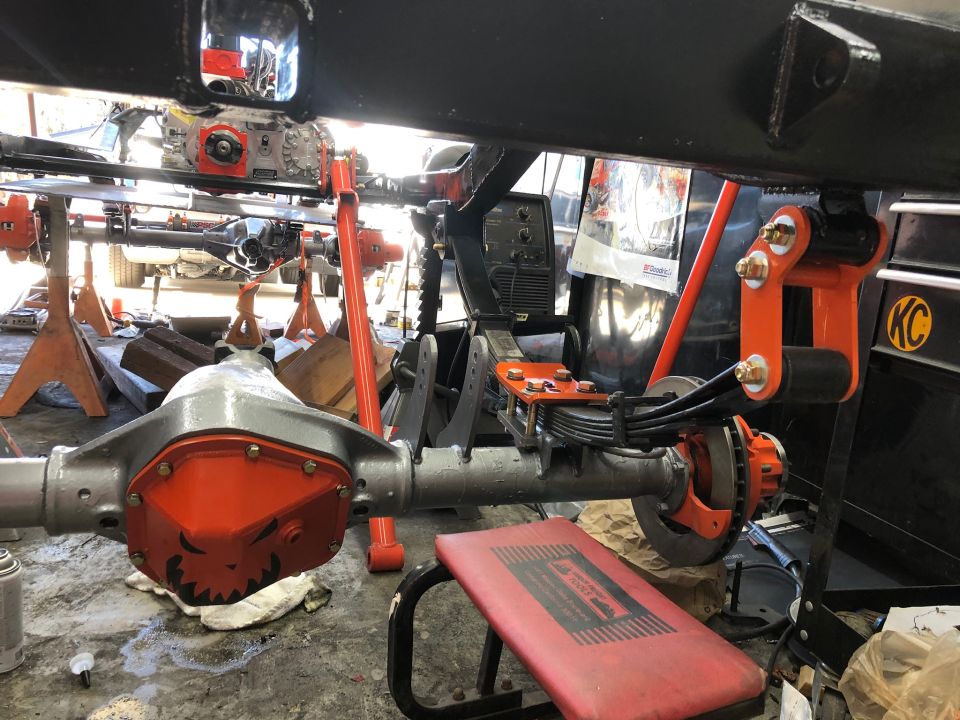 Rear axle assembly with orange differential cover and leaf springs, on jack stands
