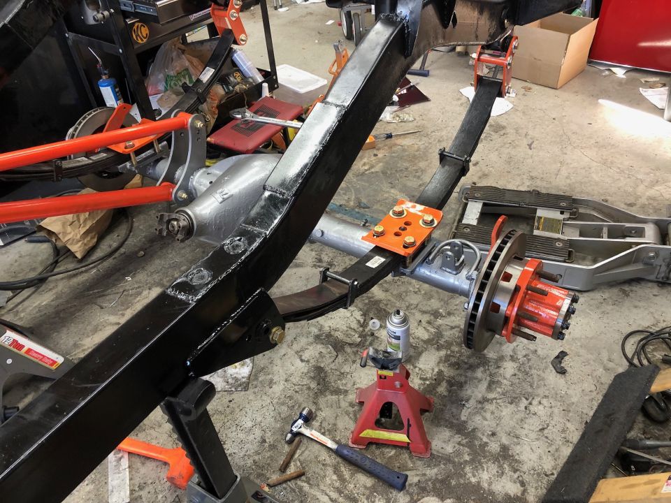 Vehicle chassis with leaf springs, brake rotor, and orange hub assembly on jack stands