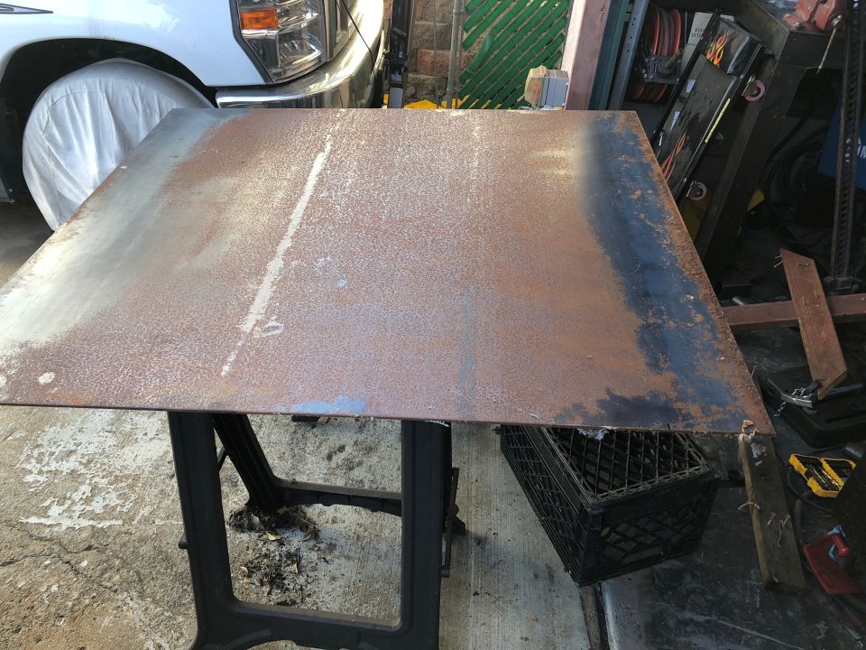 Rusted metal sheet on a black stand, with a white truck partially visible behind it