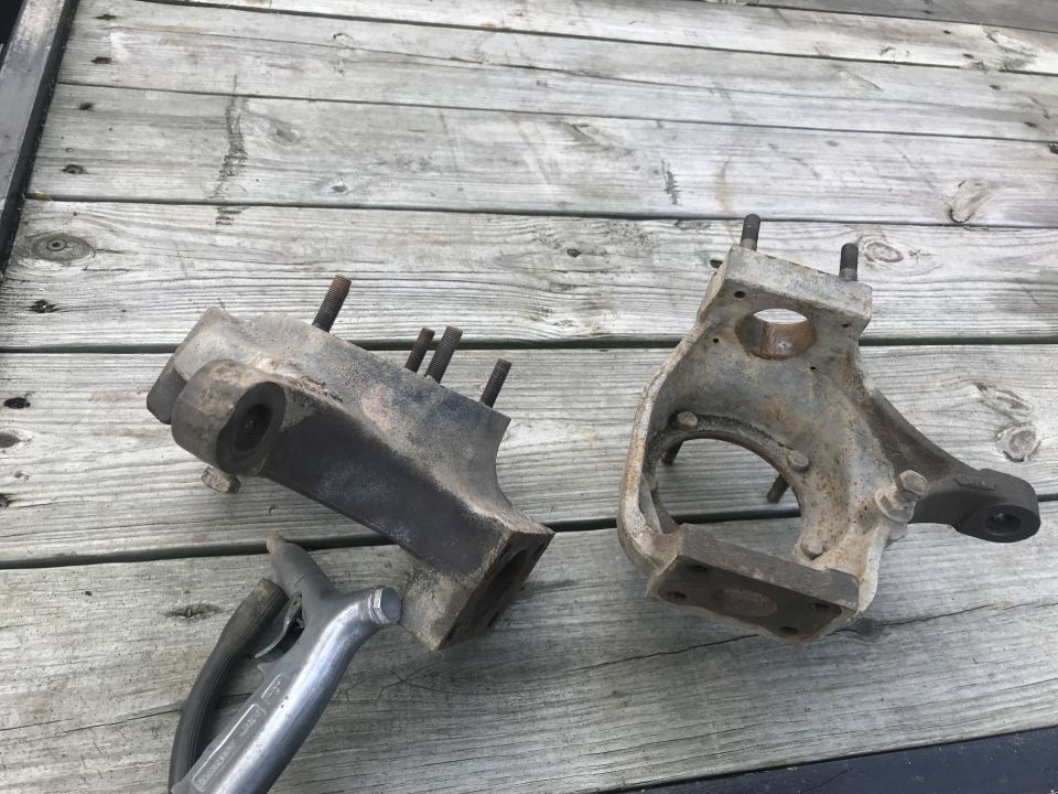 Two rusty metal vehicle suspension components on a wooden surface