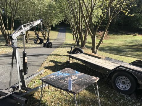 1989 Ford Bronco - An engine hoist, a flatbed trailer, and a weathered table are set up outdoors on a paved path.