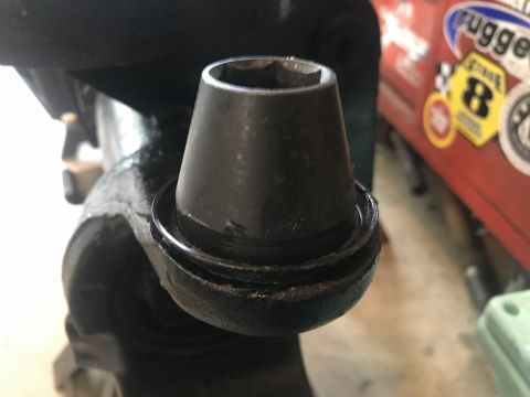 1989 Ford Bronco - Close-up of a black automotive ball joint with a socket on top, with a red vehicle in the background.