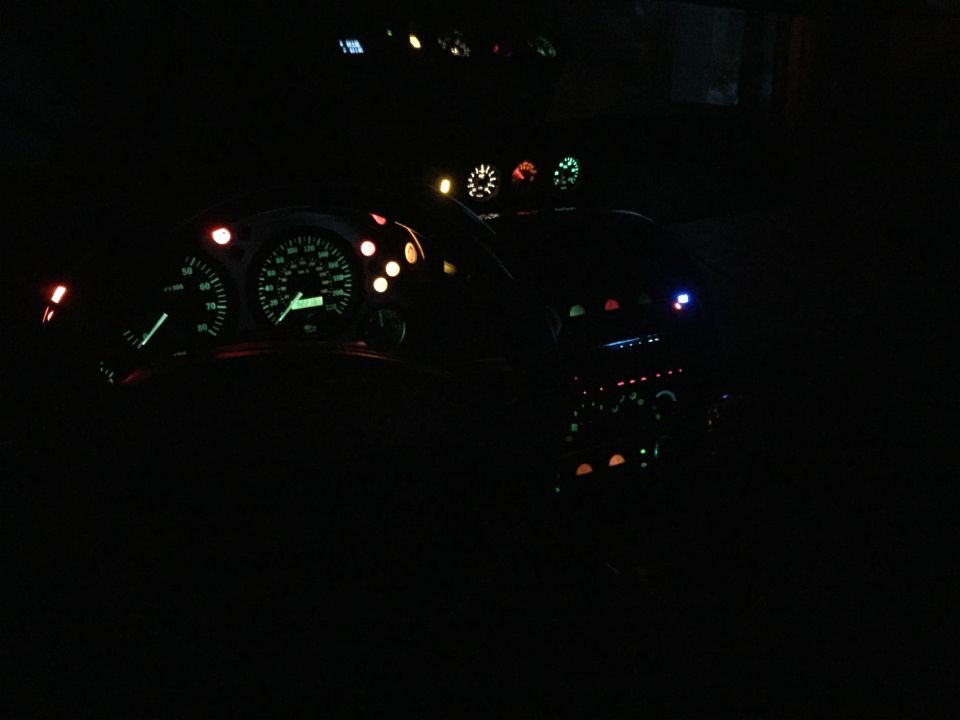 Car dashboard at night, showing illuminated speedometer, tachometer, and auxiliary gauges. Center console with buttons and lights is also visible