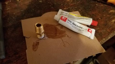 1985 Ford Bronco - Quick setting epoxy and a brass fitting are laid out on a piece of cardboard.