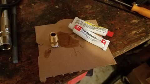 1985 Ford Bronco - Two tubes of "Epoxy - Quick Setting" and a brass fitting are on a piece of cardboard.