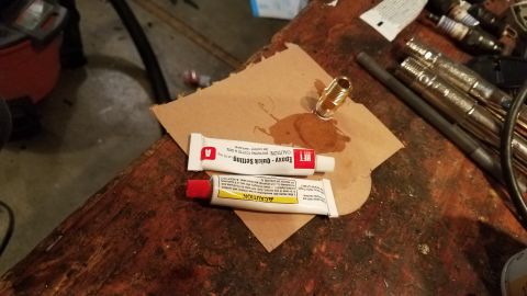 1985 Ford Bronco - Epoxy tubes and a brass fitting are laid out on a workbench, suggesting a repair or custom part assembly.