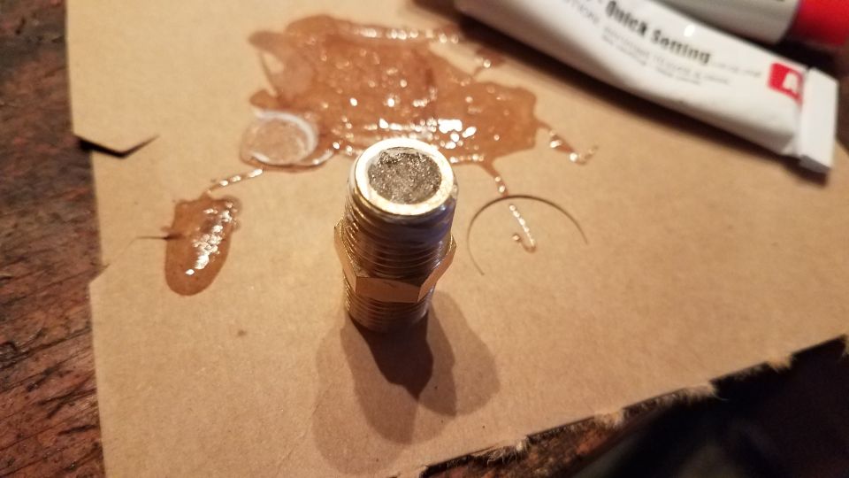 Metal fitting with adhesive on cardboard, next to a tube of quick-setting adhesive