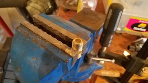 1985 Ford Bronco - A brass fitting is secured in a blue vise on a workbench.