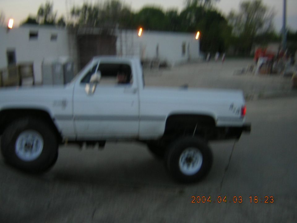 White pickup truck, side view, lifted suspension, large tires, blurry motion