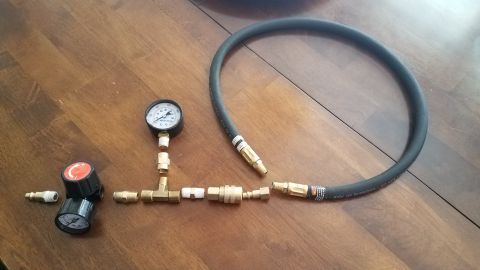 1985 Ford Bronco - A homemade leakdown tester, assembled from gauges, a regulator, brass fittings, and a hose, lies on a wooden table.