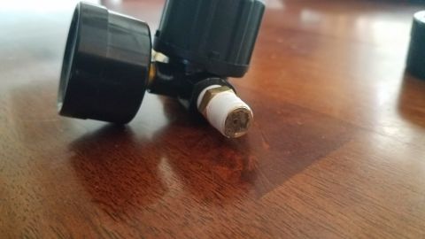 1985 Ford Bronco - Close-up of an air pressure regulator with a threaded connection, resting on a wooden surface.