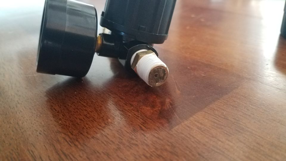 Black gauge with white threaded fitting on wooden surface