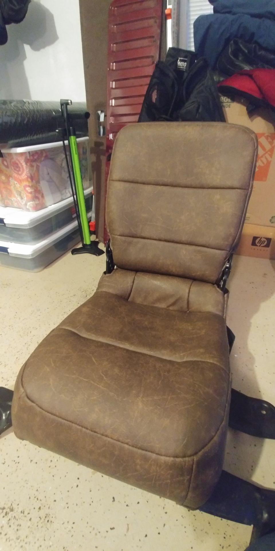 Brown distressed vinyl center jump seat with black brackets sitting on a garage floor among storage bins and boxes