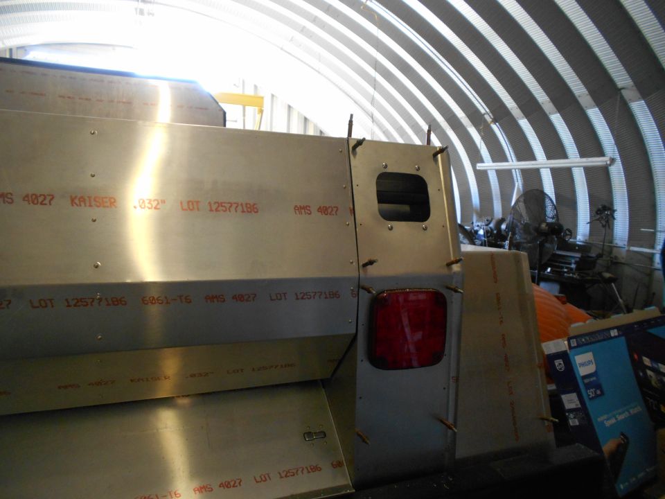 Back corner of a vehicle under construction, showing metal panels with red markings and a taillight