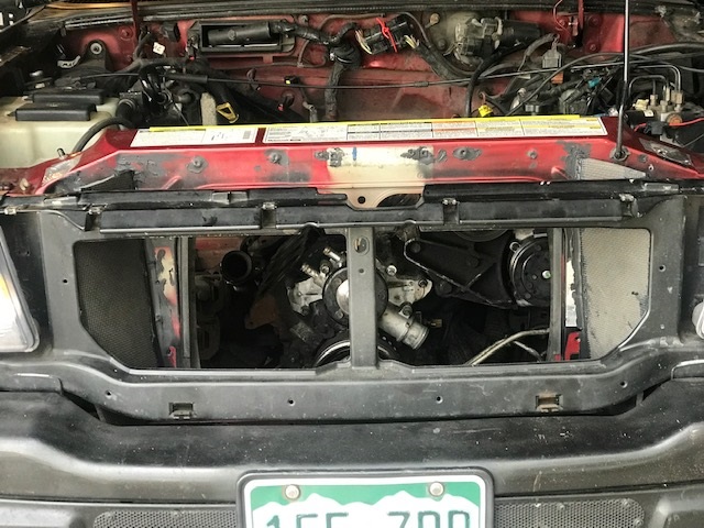 Red vehicle engine bay with radiator removed, showing engine components and black grille
