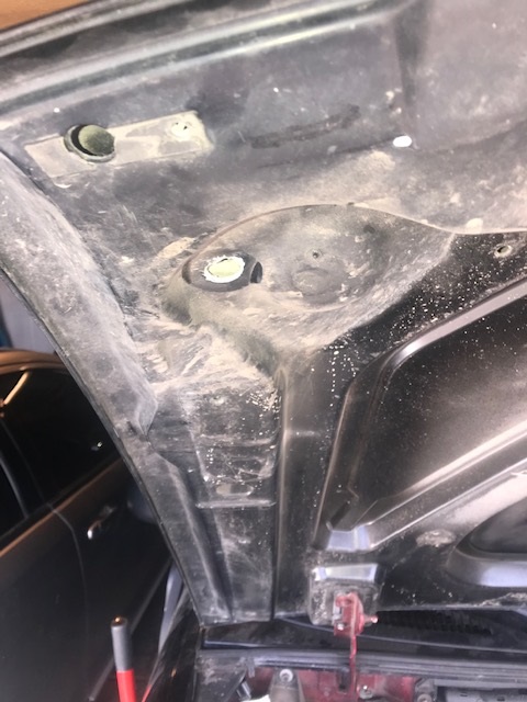 2000 Ford Explorer - The underside of a car hood shows mounting points and accumulated dust, with a partial view of another vehicle in the background.