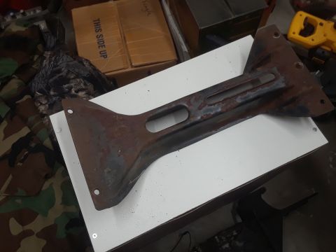 1994 Ford Bronco - A heavily rusted metal bracket with a distinctive shape, likely a component from a vehicle's chassis or suspension system.