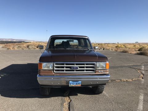 1988 Ford Bronco - This Ford truck is parked in an open area under a clear blue sky.