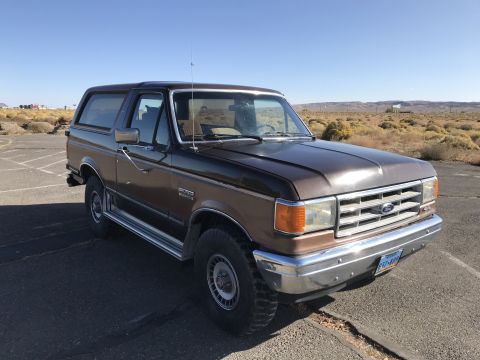 1988 Ford Bronco - A two-tone brown Ford Bronco is parked outdoors under a clear blue sky.