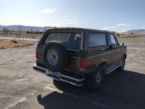 1988 Ford Bronco - Rear view of a brown Ford Bronco with a spare tire mounted on the tailgate under a clear sky.