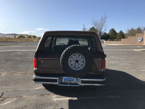 1988 Ford Bronco - Rear view of a brown Ford Bronco parked outdoors under a clear blue sky.