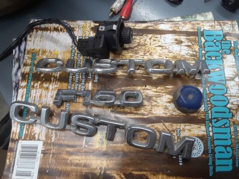 1994 Ford Bronco - Chrome emblems and a car part are laid out on a magazine cover.