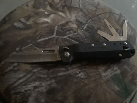 1994 Ford Bronco - A multi-tool knife with its blade and several other tools deployed is shown on a camouflage background.