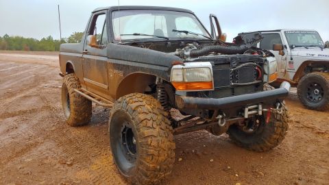 1995 Ford Bronco - Modified 1995 Ford Bronco sits in mud with its hood open, next to a white Jeep.
