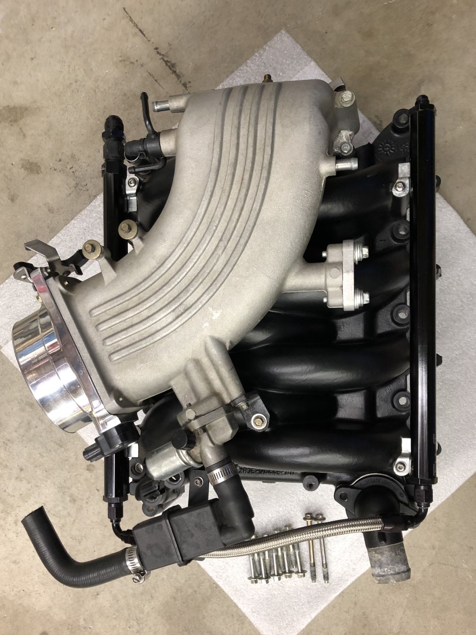 Aluminum intake manifold with throttle body and fuel rail resting on foam on a garage floor