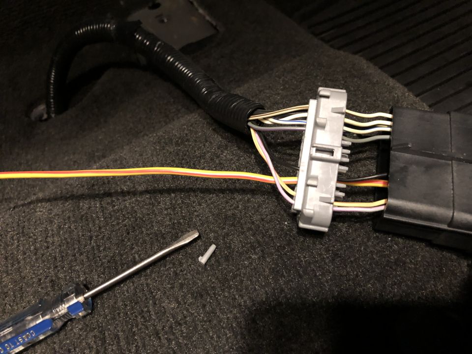 Car interior carpet with a wiring harness connector unplugged, a screwdriver, and a small plastic piece