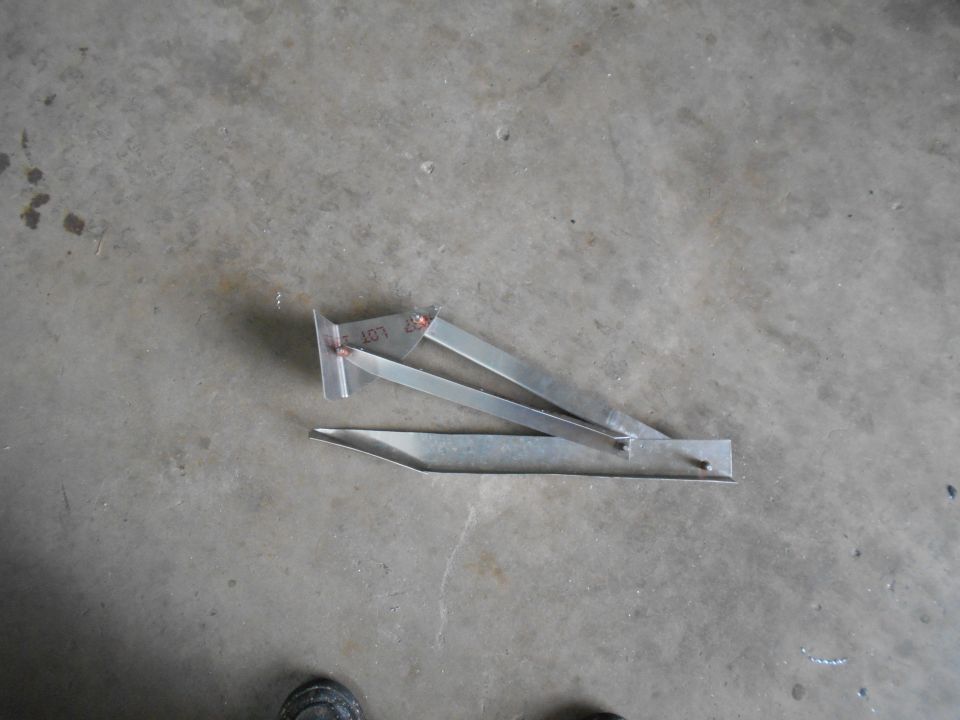 Metal bracket with some writing on it, lying on a concrete floor