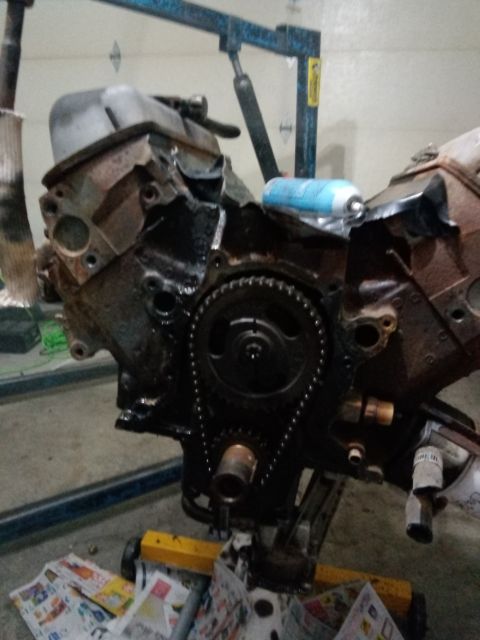 1994 Ford Bronco - Engine block assembly on a stand, with timing chain and gears exposed. A spray can is on top.